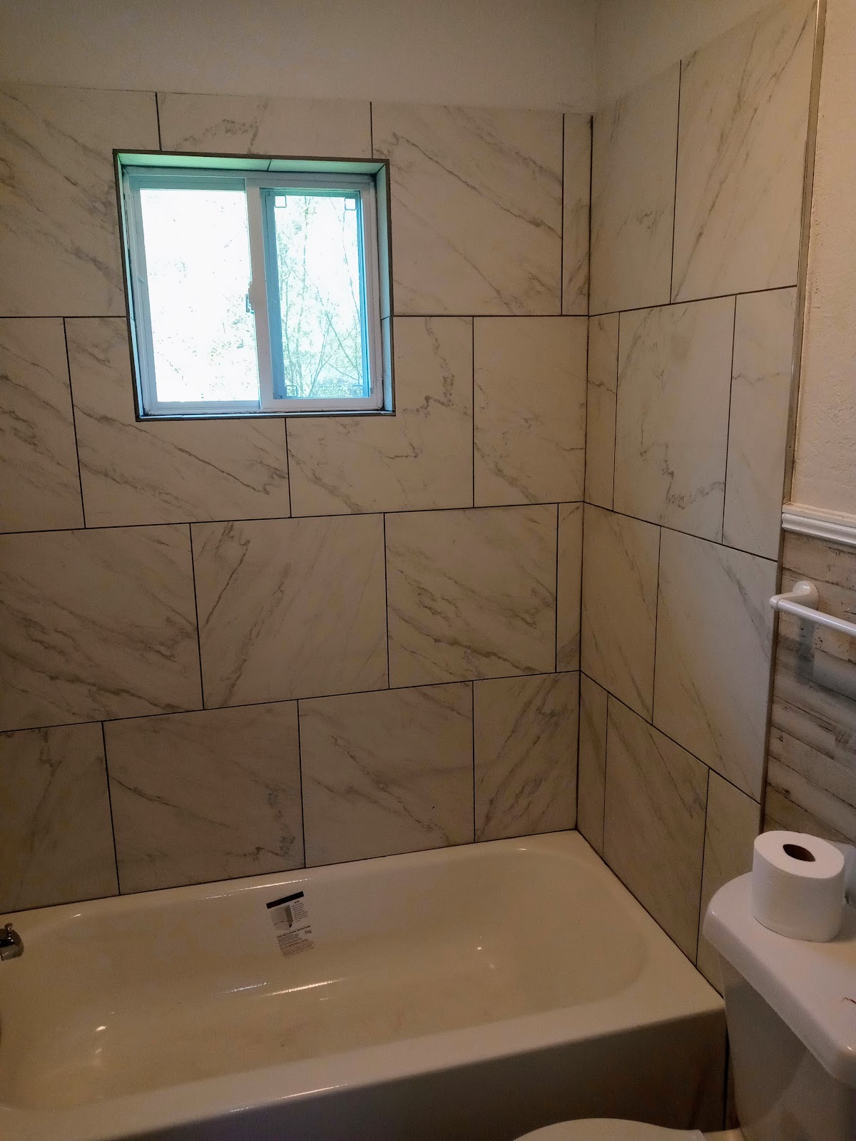 Bathtub with large marble-pattern tile surround and a window