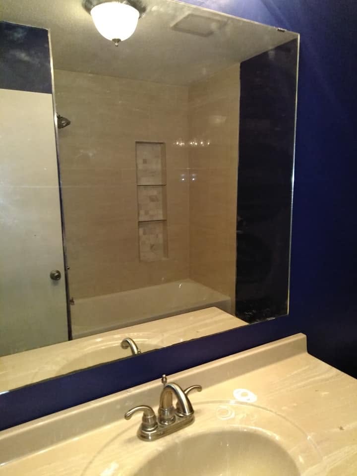 Bathroom vanity with a large frameless mirror and tiled shower niche